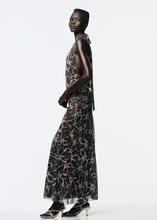 Black maxi dress with white floral pattern, halter neckline, and sleeveless design shown on model in side profile.
