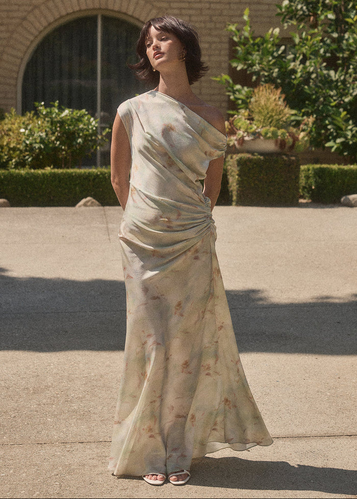Cream maxi dress with ruched side detailing and subtle floral print, worn with slide sandals.