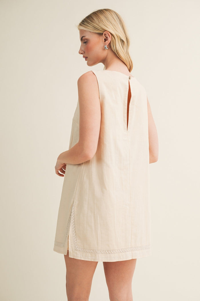 Cream sleeveless dress romper with open back detail and lace trim at hem, shown from behind on model.