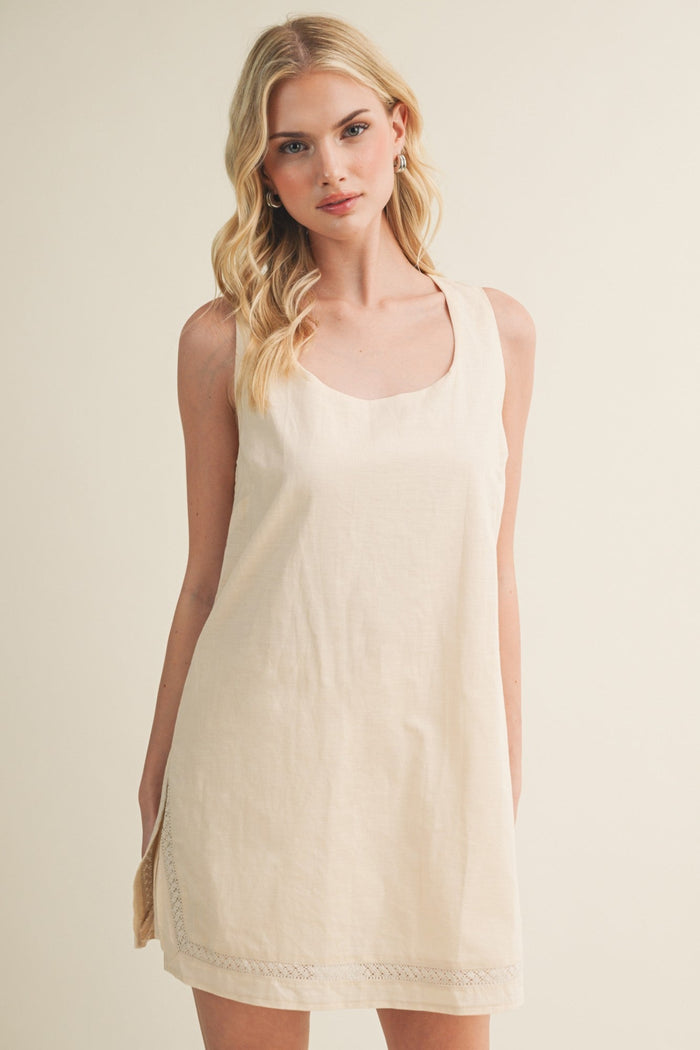 Cream sleeveless dress romper with lace trim at hem, scoop neckline, modeled on woman against beige background.