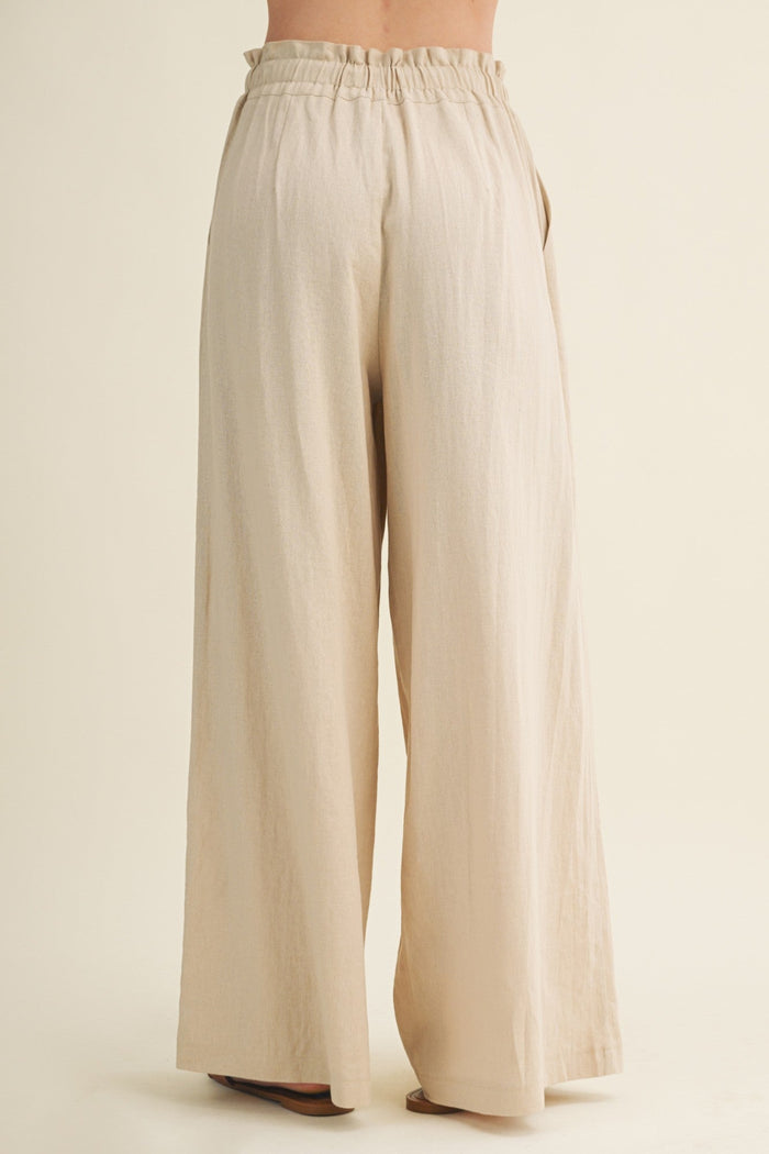 Beige wide-leg pants with an elastic waistband, viewed from behind on a model wearing brown shoes.