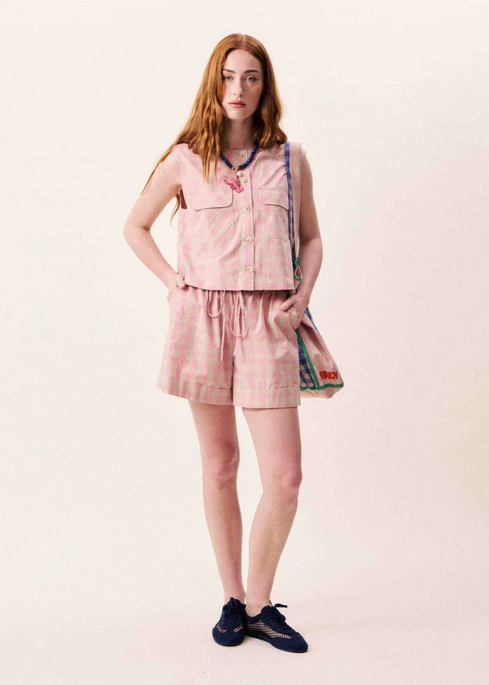 Pink sleeveless button-front vest with chest pockets and matching drawstring shorts, styled with a crossbody bag.