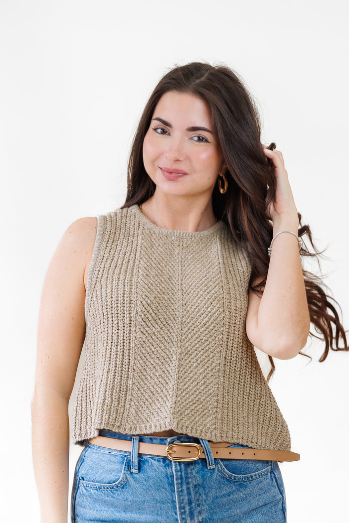 Beige sleeveless knit top with ribbed texture worn with blue jeans and tan belt.