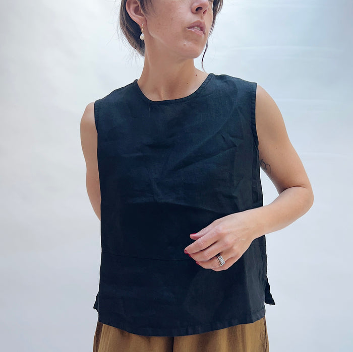 Close front view of model wearing Bryn Walker black basic linen tank, showing crew neckline, sleeveless cut, relaxed boxy fit, side slits, and black color, styled with camel wide-leg pants
