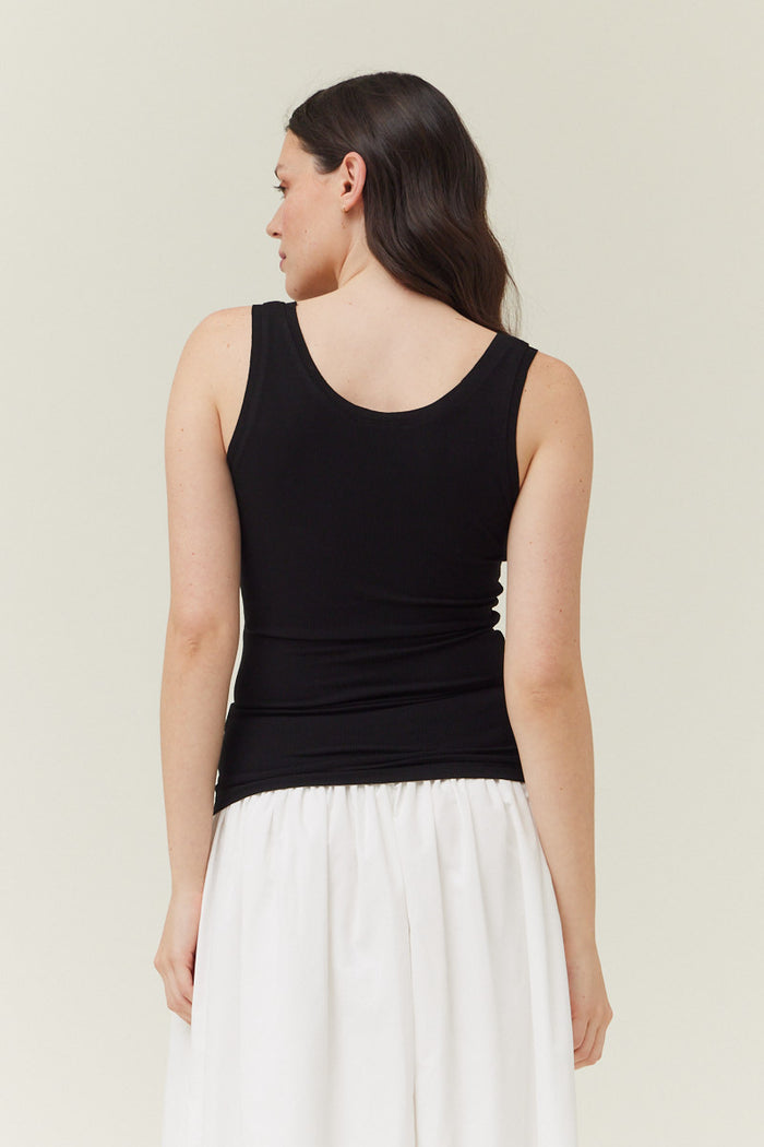 Black ribbed sleeveless tank top with scoop neckline worn with white skirt, shown from back view.