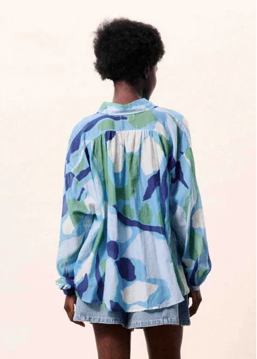 Person wearing a colorful shirt standing in front of a blue vase on a beige surface.
