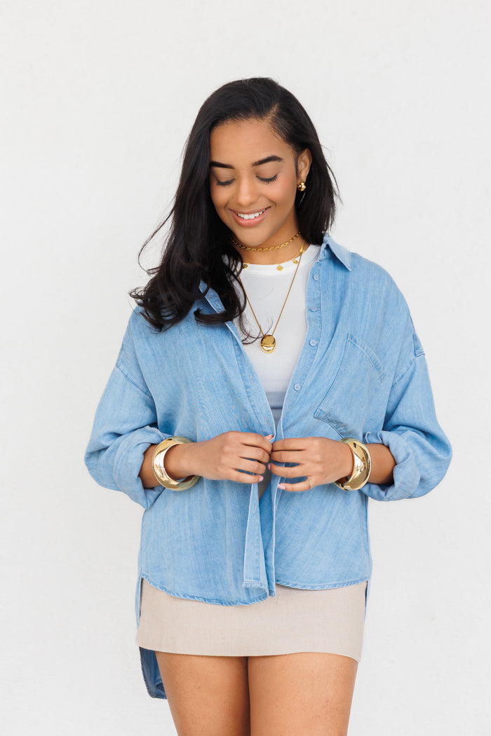 Light blue chambray button-up shirt with long sleeves and front pocket detail.