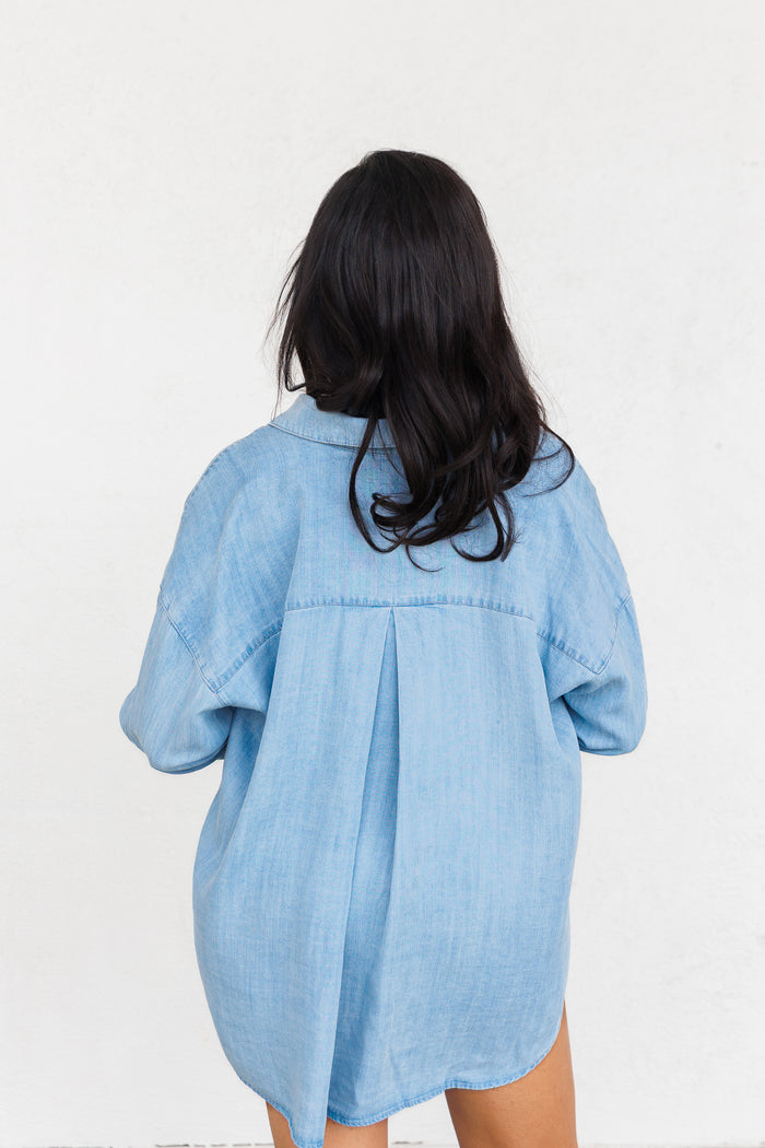 Light blue chambray shirt dress with three-quarter sleeves and pleated back detail, shown from behind.