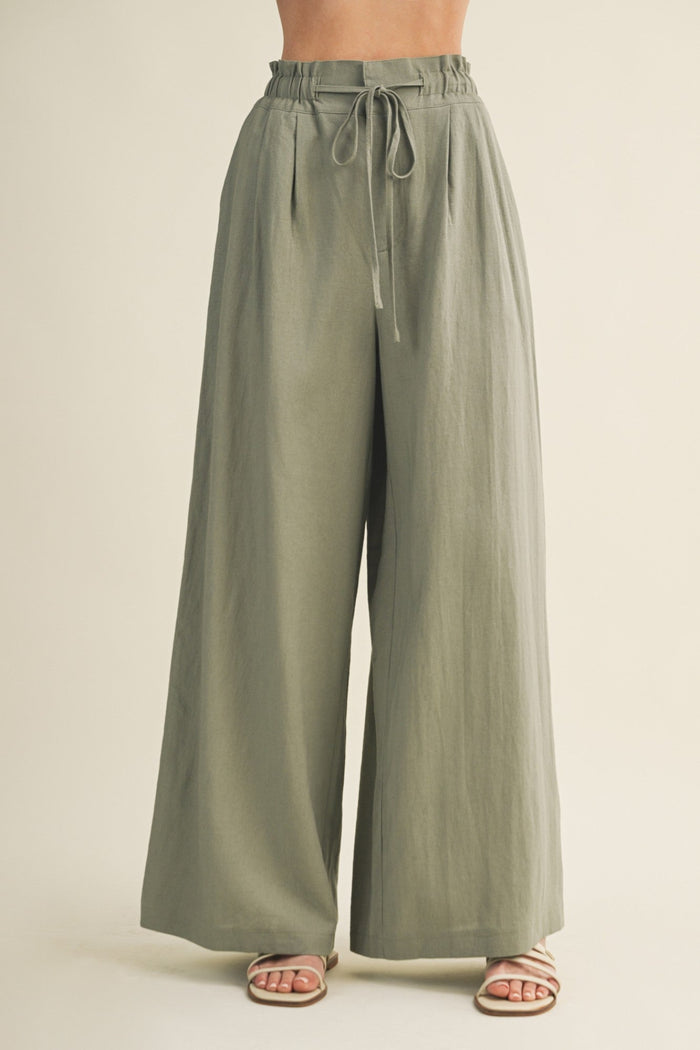 Sage green wide-leg pants with elastic waistband and drawstring tie, shown on model wearing sandals.