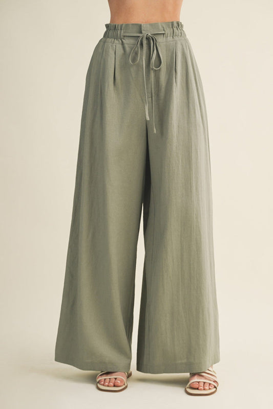 Sage green wide-leg pants with elastic waistband and drawstring tie, shown on model wearing sandals.