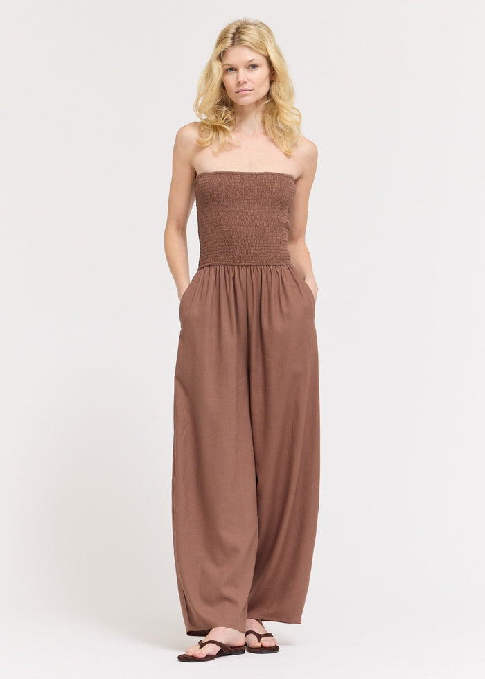 Taupe strapless jumpsuit with smocked bodice, flowing wide legs, and side pockets.