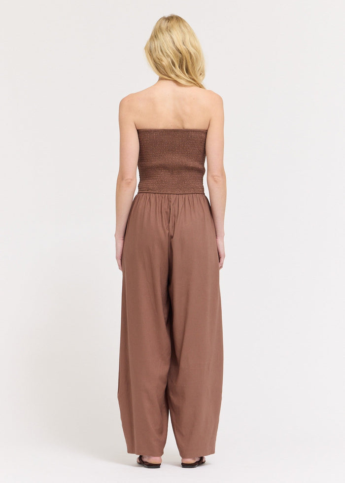 Brown strapless jumpsuit with ruched bodice and wide-leg pants with cocoon hem, shown on model from back.