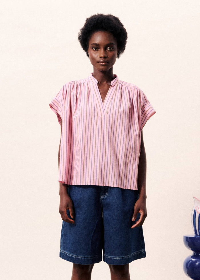 Pink vertical striped short-sleeve top with V-neckline worn with dark blue denim shorts.