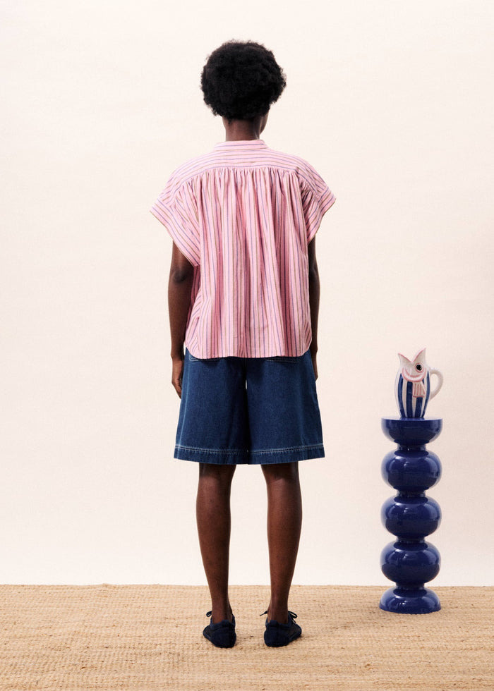 Pink and white striped short-sleeve top with pleated back, worn with denim shorts.