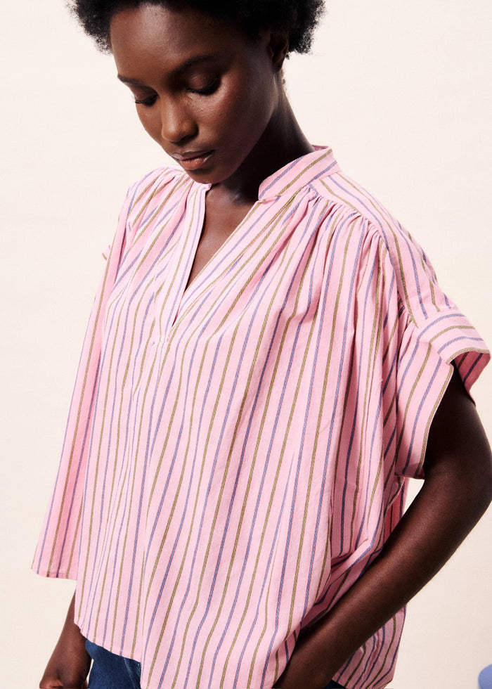 Pink short sleeve top with purple, white, and gold vertical stripes and V-neckline.