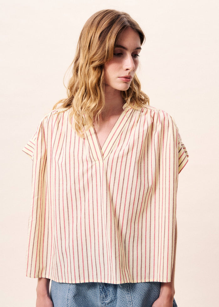 Woman wearing short-sleeve top with pink and cream vertical stripes and V-neckline, paired with light blue jeans.