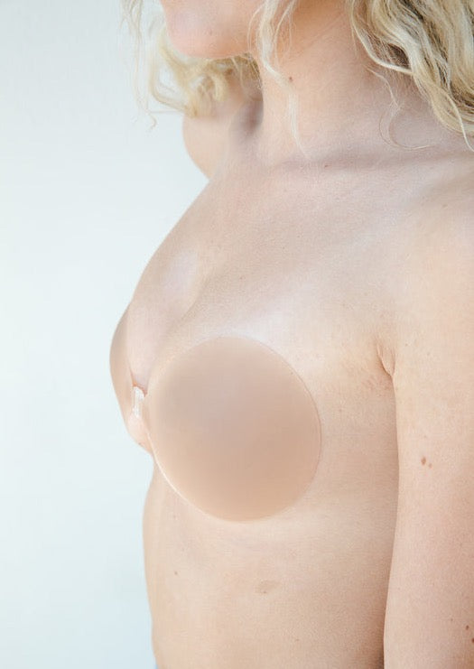 Adhesive nude breast cover shown applied on model's chest in profile view.