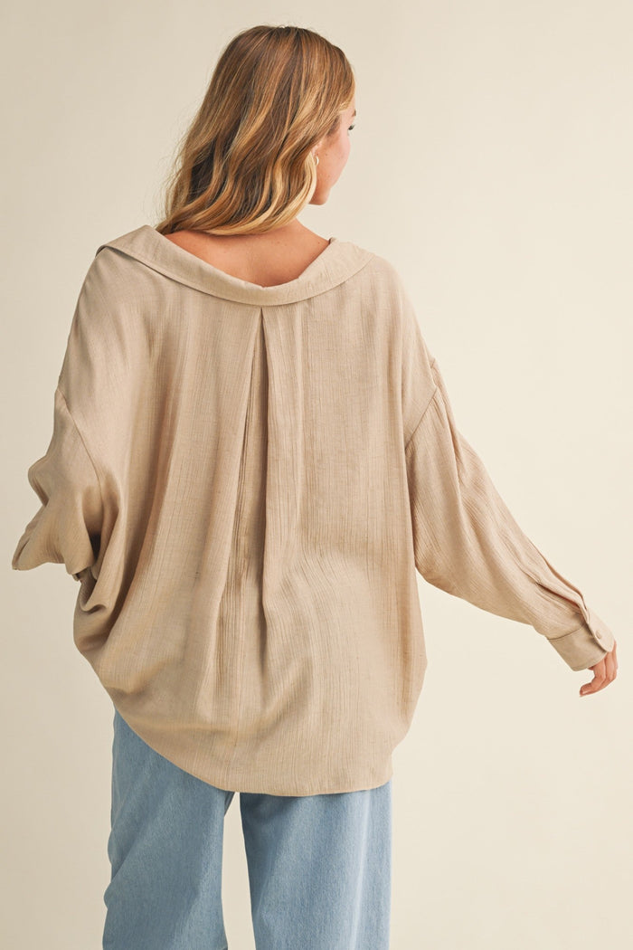 Beige button-down top with voluminous sleeves and draped collar, worn with light blue jeans.