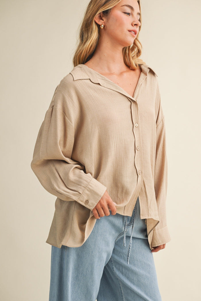 Beige button-down top with relaxed fit, collared neckline, and long sleeves, worn with blue jeans.