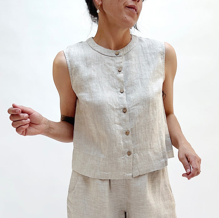 A close up shot of a person with her hands at either side of her wearing a matching button front linen tank in beige with beige linen pants.
