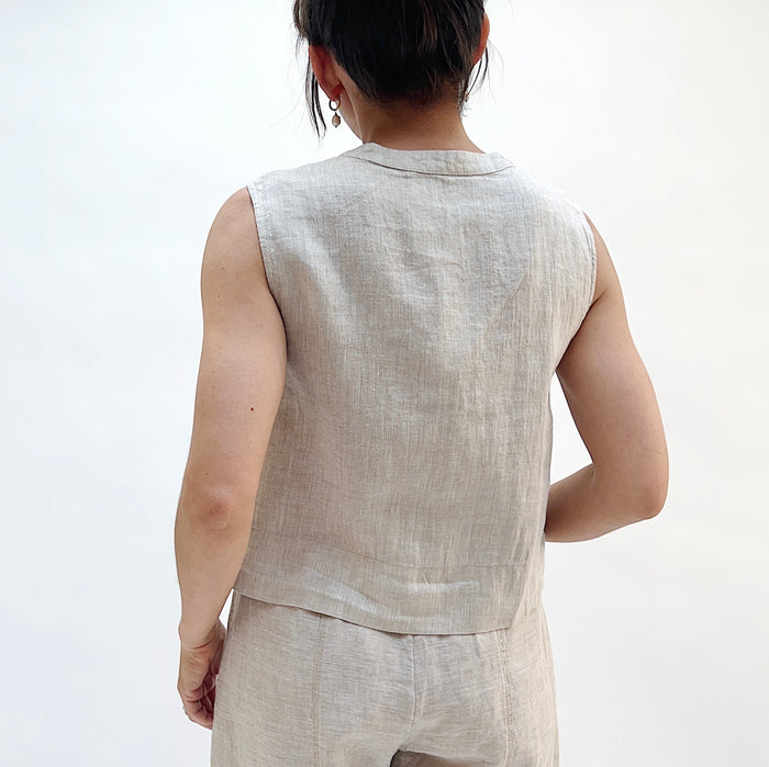 A close up shot of a person seen from behind wearing a matching button front linen tank in beige with beige linen pants.