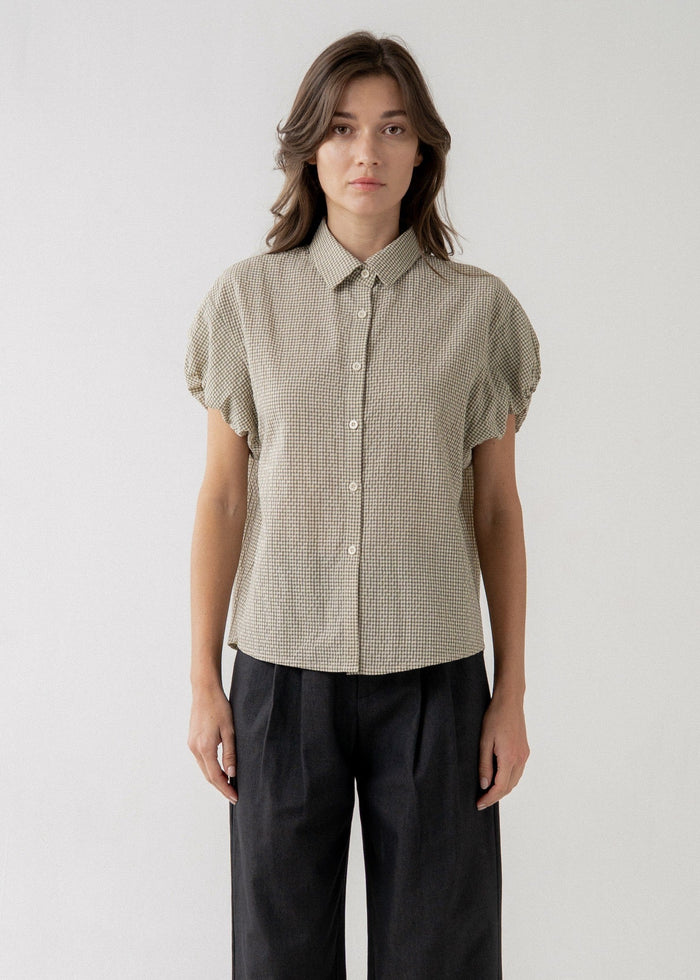 Beige textured button-front blouse with short puffed sleeves and collared neckline worn with black pants.