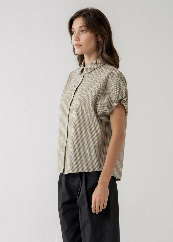 Beige textured short-sleeve blouse with puff sleeves and collar, worn with black trousers.