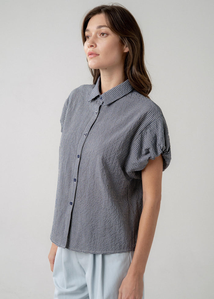 Blue and white checkered button-up blouse with short puffed sleeves and a collared neckline.