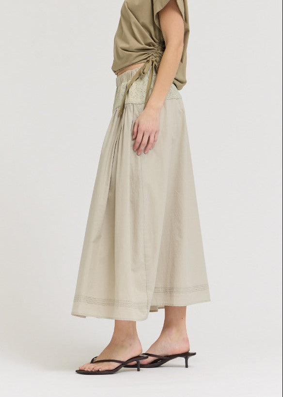 Woman wearing a green top and beige skirt on a white background