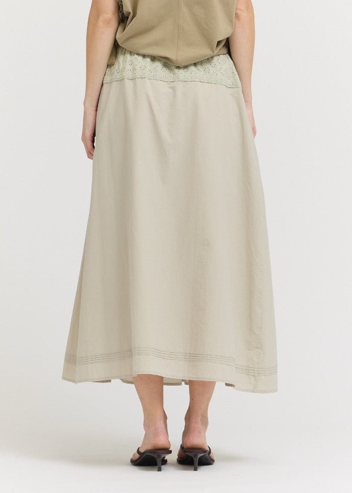 Person wearing a beige skirt and top on a white background