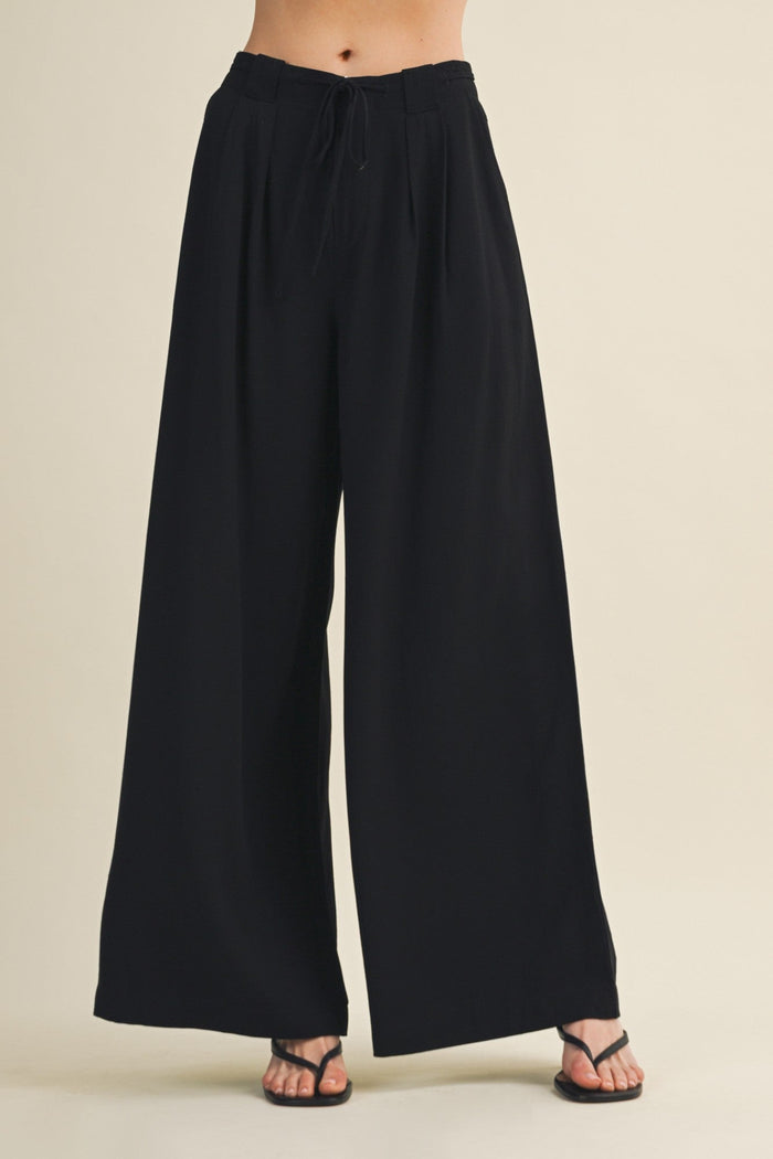 Black wide-leg pants worn by a person on a beige background
