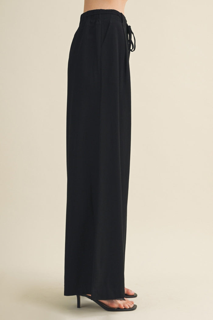 Black wide-leg pants worn by a person on a beige background