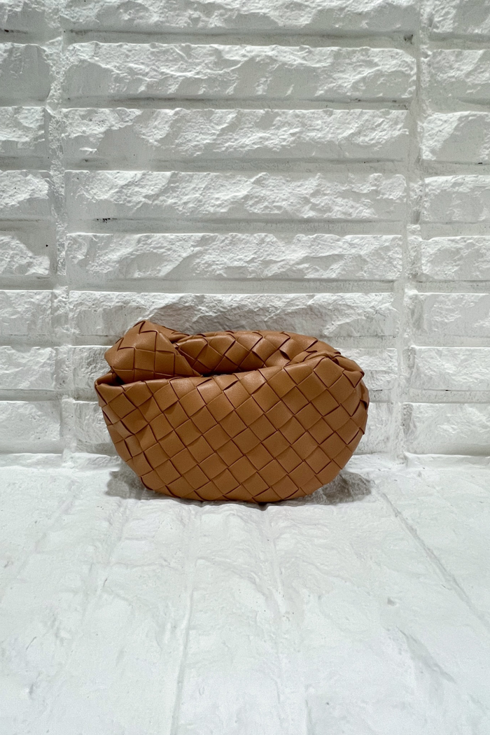 Tan leather handbag with quilted diamond pattern and gathered top, displayed against white brick background.