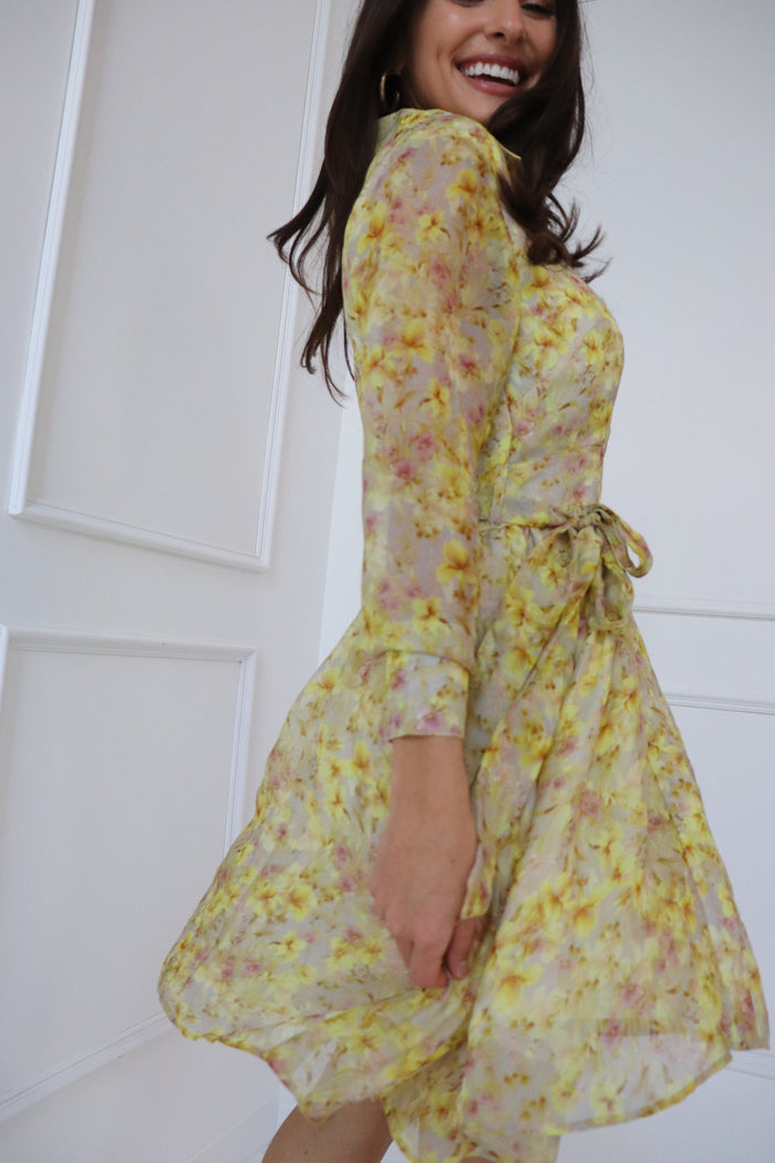 Yellow floral wrap dress with three-quarter sleeves and tied waist detail on model.