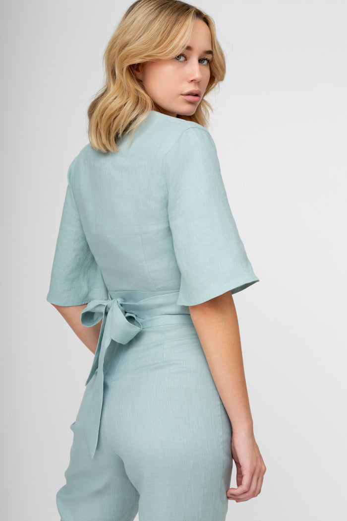 Light blue linen wrap top with short flutter sleeves and tied waist detail, shown from back view.