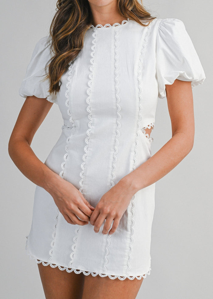 White mini dress with puffed sleeves, lace trim details, and vertical lace panels on front.