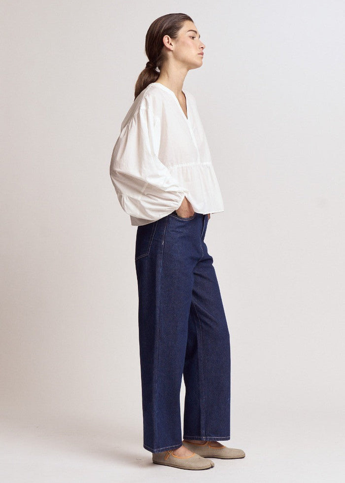 Woman wearing white blouse with puffy sleeves and dark blue jeans, shown in profile view.