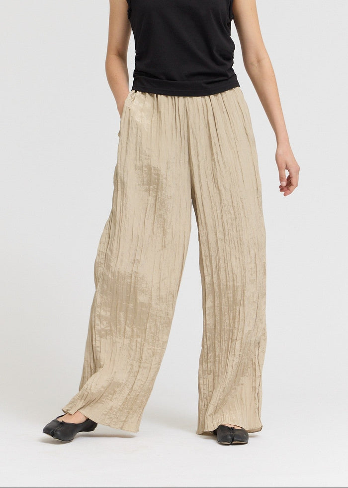 Woman wearing a black sleeveless top and beige pleated pants on a white background
