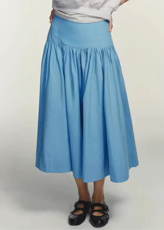 Blue midi skirt with gathered waistband and full skirt silhouette, worn with gray sweater.