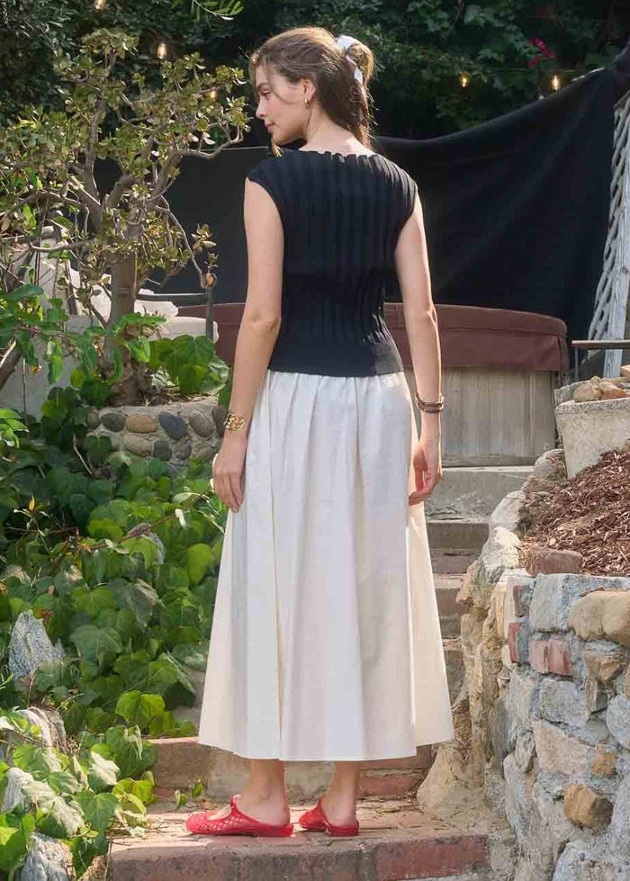 Black sleeveless ribbed top with white pleated midi skirt, worn with red flat sandals.