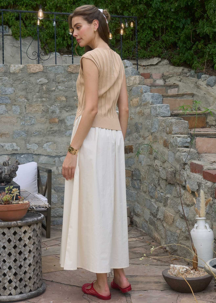 Beige sleeveless top with vertical pleats and cream midi skirt on model standing outdoors.