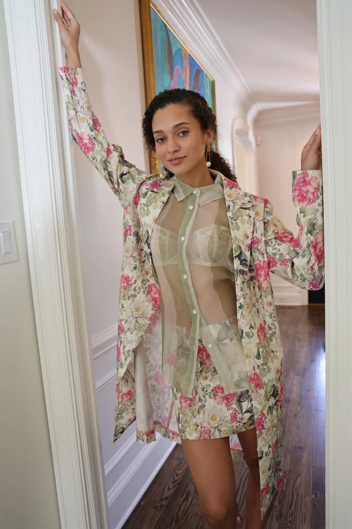 Woman wearing cream mini skirt with floral print cardigan and sheer button-up shirt.