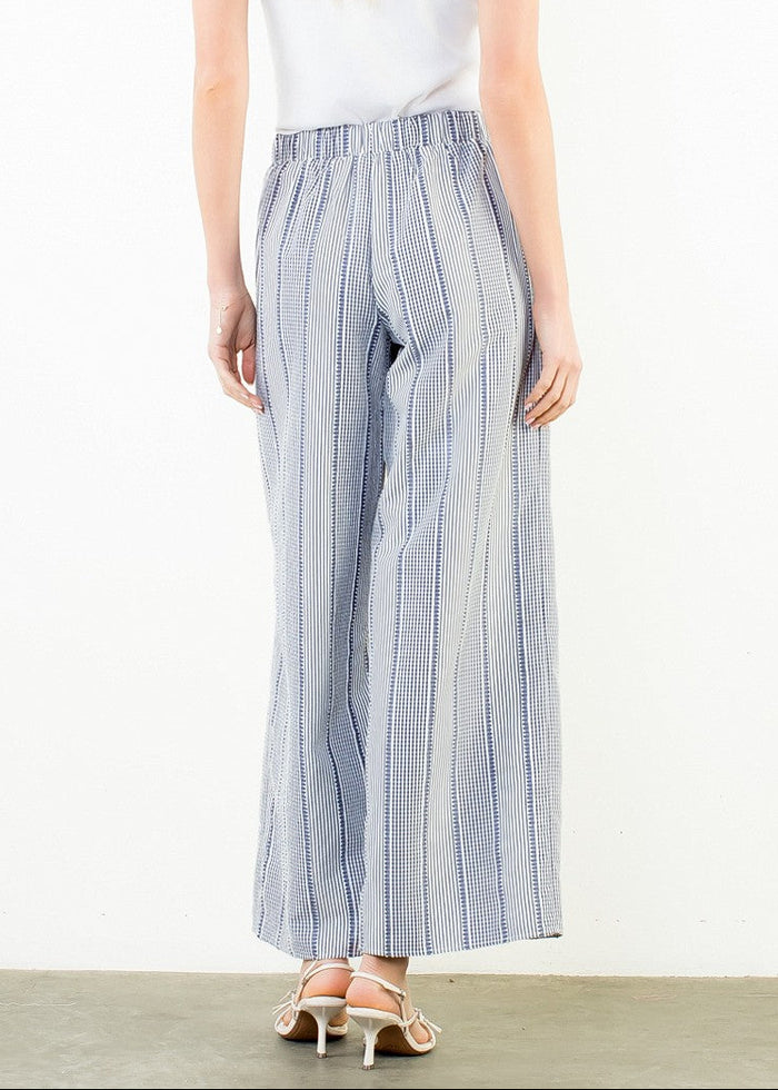 Woman wearing blue striped pants and a white top on a plain background