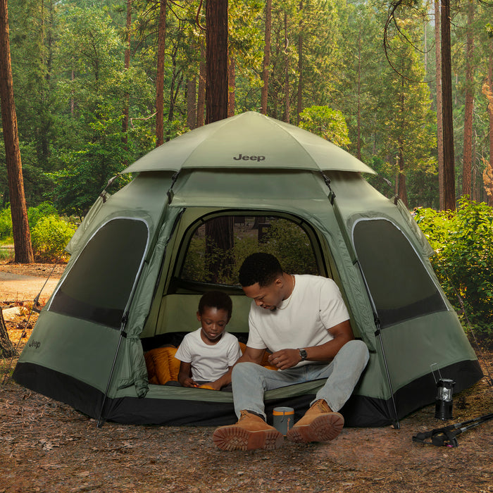 Man and child sitting inside a green Jeep tent in a forest setting