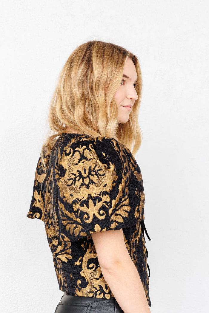 Black and gold jacquard top with ornate floral pattern and short sleeves, shown from back view on model.