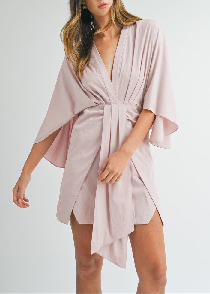 Blush pink wrap mini dress with draped flutter sleeves and asymmetrical hemline.