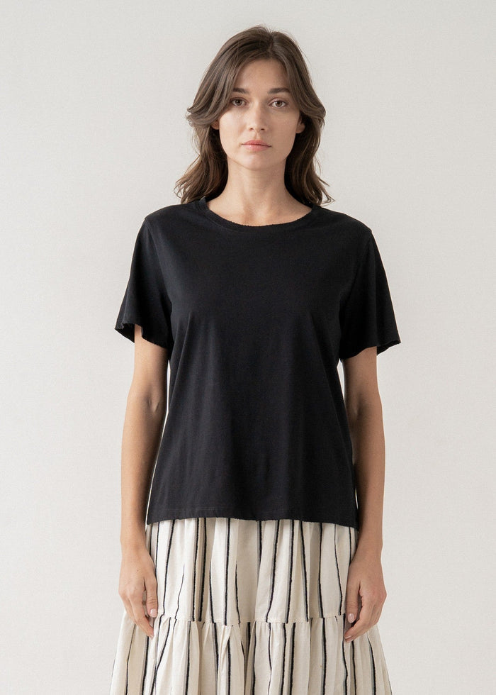Woman wearing black short-sleeve t-shirt with crew neckline over striped tiered skirt.