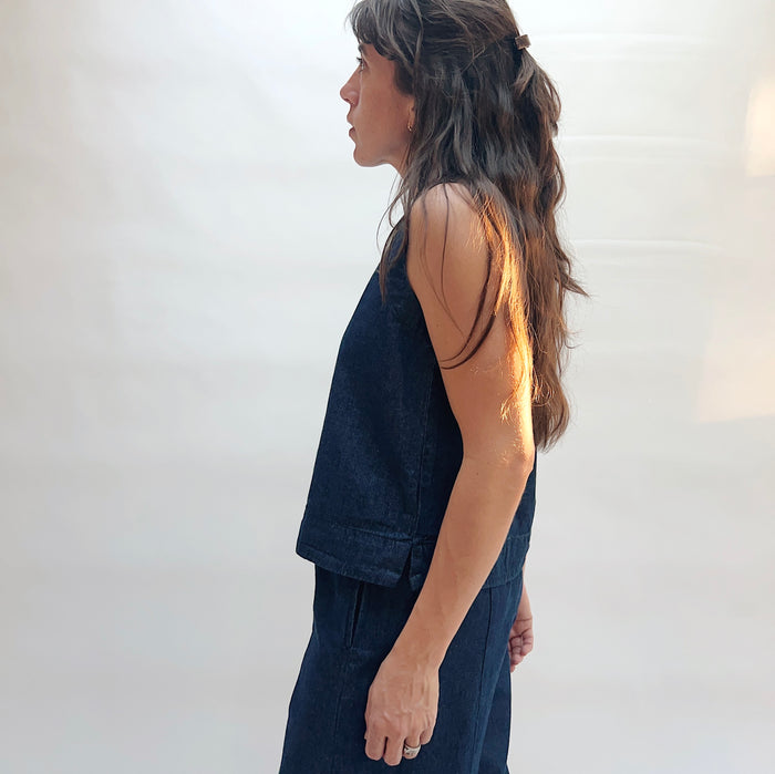 Woman wearing a dark blue sleeveless top and pants against a white background