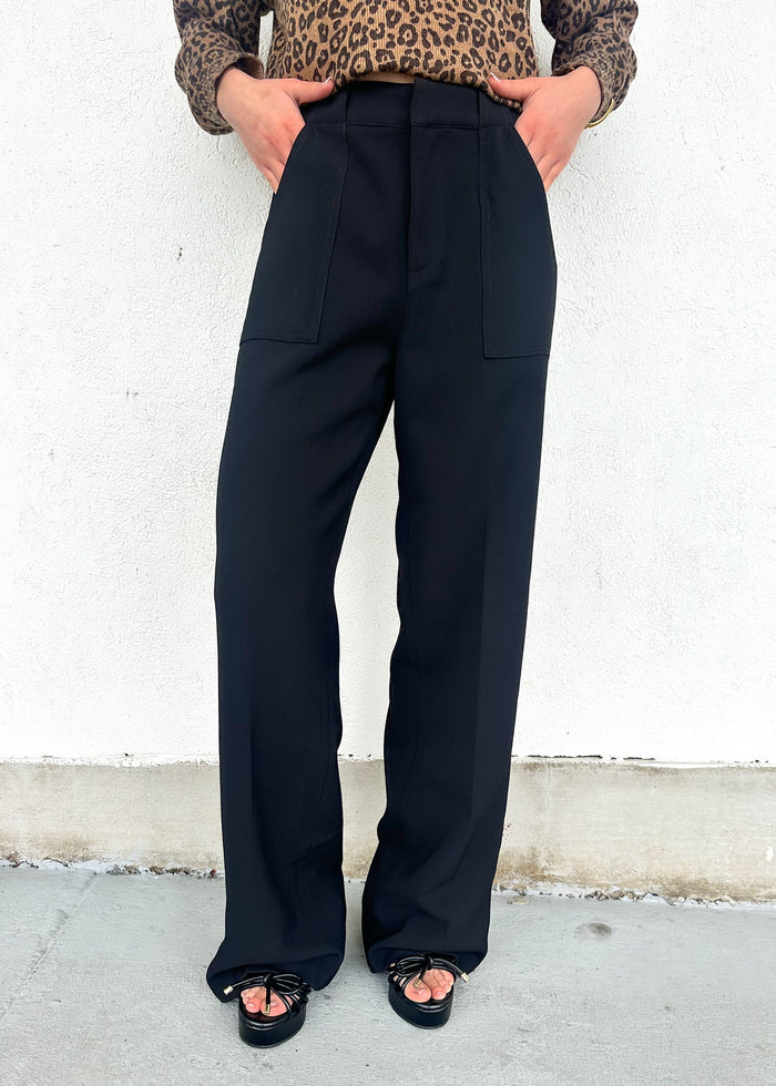 Person wearing black high-waisted pants with a leopard print top against a white wall.