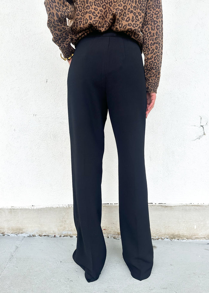 Person wearing black pants and a leopard print top against a white wall.